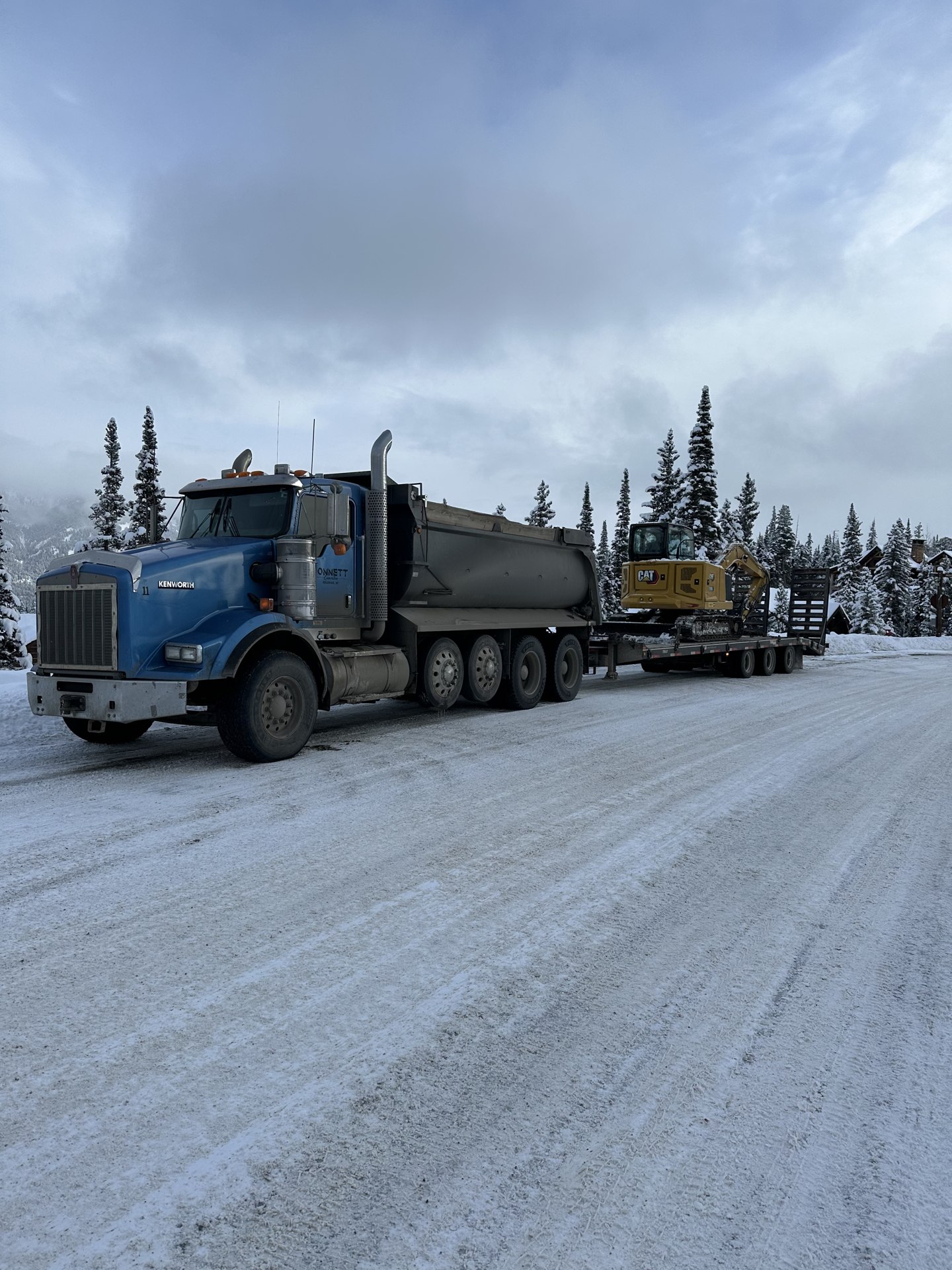 Monnett truck hauling an excavator on a trailer along a snowy road