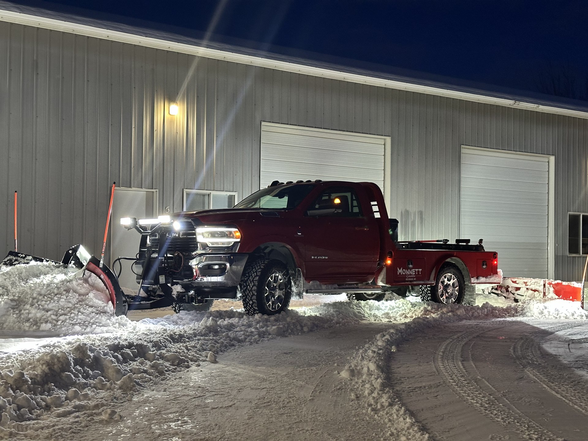 Monnett snowplow truck clearing snow outside a building at night