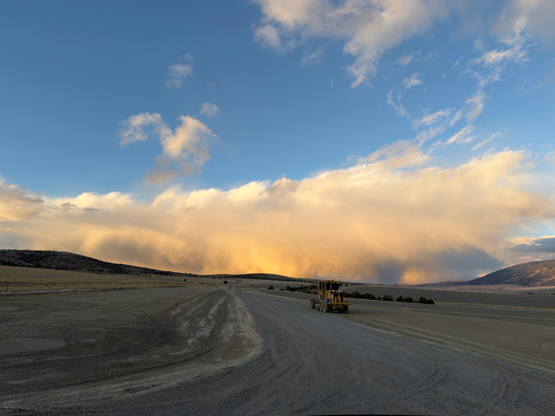 Monnett road grader beside a newly built road beneath a Montana evening sky
